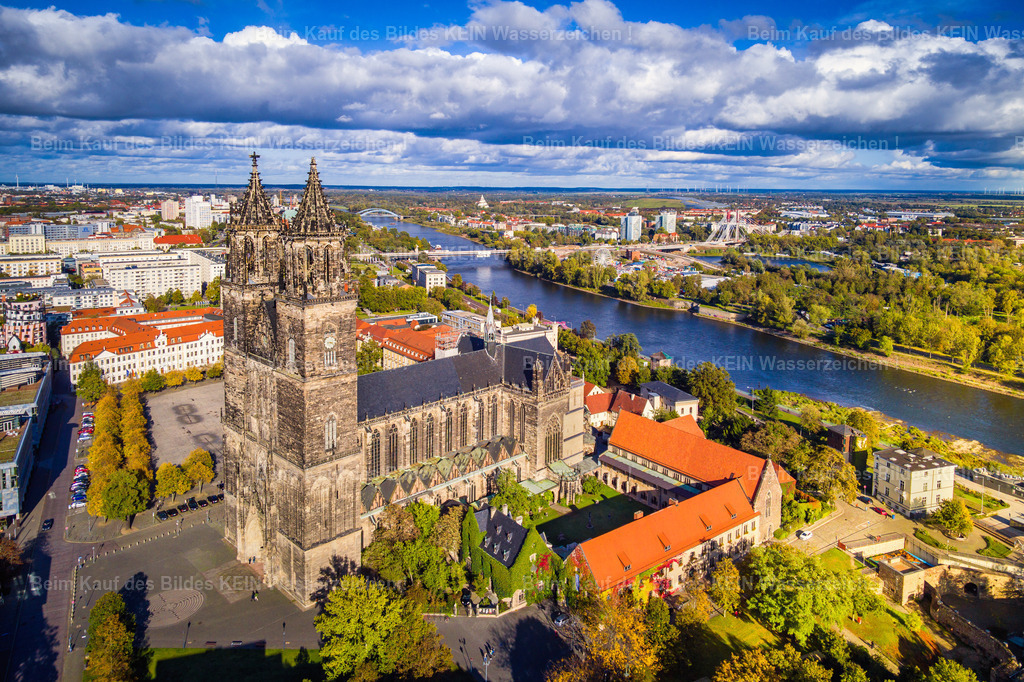 Luftbild Magdeburg Dom neu im Herbst und Elbe-0047 | Der Magdeburger Dom und die Elbe prägen diese Luftaufnahme der Innenstadt im Herbst. Im Vordergrund erhebt sich der Dom St. Mauritius und Katharina mit seinen markanten Doppeltürmen. Rund um das historische Bauwerk liegen die Domplatzbebauung, die roten Ziegeldächer und weitere Gebäude der Magdeburger Altstadt. Die herbstlich gefärbten Bäume entlang der Elbe setzen farbige Akzente im Stadtbild. –  – Hinter dem Dom öffnet sich der Blick über die Elbe auf das gegenüberliegende Ufer mit dem weitläufigen Stadtpark Rotehorn. Die Strombrücke und weitere Teile der Stadtlandschaft verbinden die beiden Elbseiten. Aus der Vogelperspektive werden die Lage des Doms direkt am Fluss und die räumliche Struktur der Innenstadt besonders deutlich. –  – Der Magdeburger Dom gilt als erster gotischer Kathedralbau auf deutschem Boden. Er wurde im Jahr 1209 begonnen und prägt bis heute die Silhouette der Landeshauptstadt Sachsen-Anhalts. Mit seinen beiden rund 100 Meter hohen Türmen ist er weithin sichtbar und zählt zu den bedeutendsten historischen Bauwerken der Region. –  – Die Aufnahme vermittelt einen Überblick über Magdeburgs Innenstadt und ihre markante Lage an der Elbe. Historische Architektur, Flusslandschaft, Grünflächen und moderne Stadtbereiche bilden gemeinsam das Stadtbild. Die herbstlichen Farben und die eindrucksvollen Wolkenformationen geben dieser Ansicht eine besondere Atmosphäre, ohne den Blick auf die Stadt und ihre räumliche Struktur in den Hintergrund zu rücken. - Realisiert mit Pictrs.com